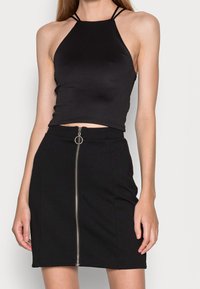 Top corto negro con cuello halter y tirantes finos, combinado con una falda negra que cuenta con un zipper frontal y un tirador en forma de anillo. Ambos artículos son ajustados.