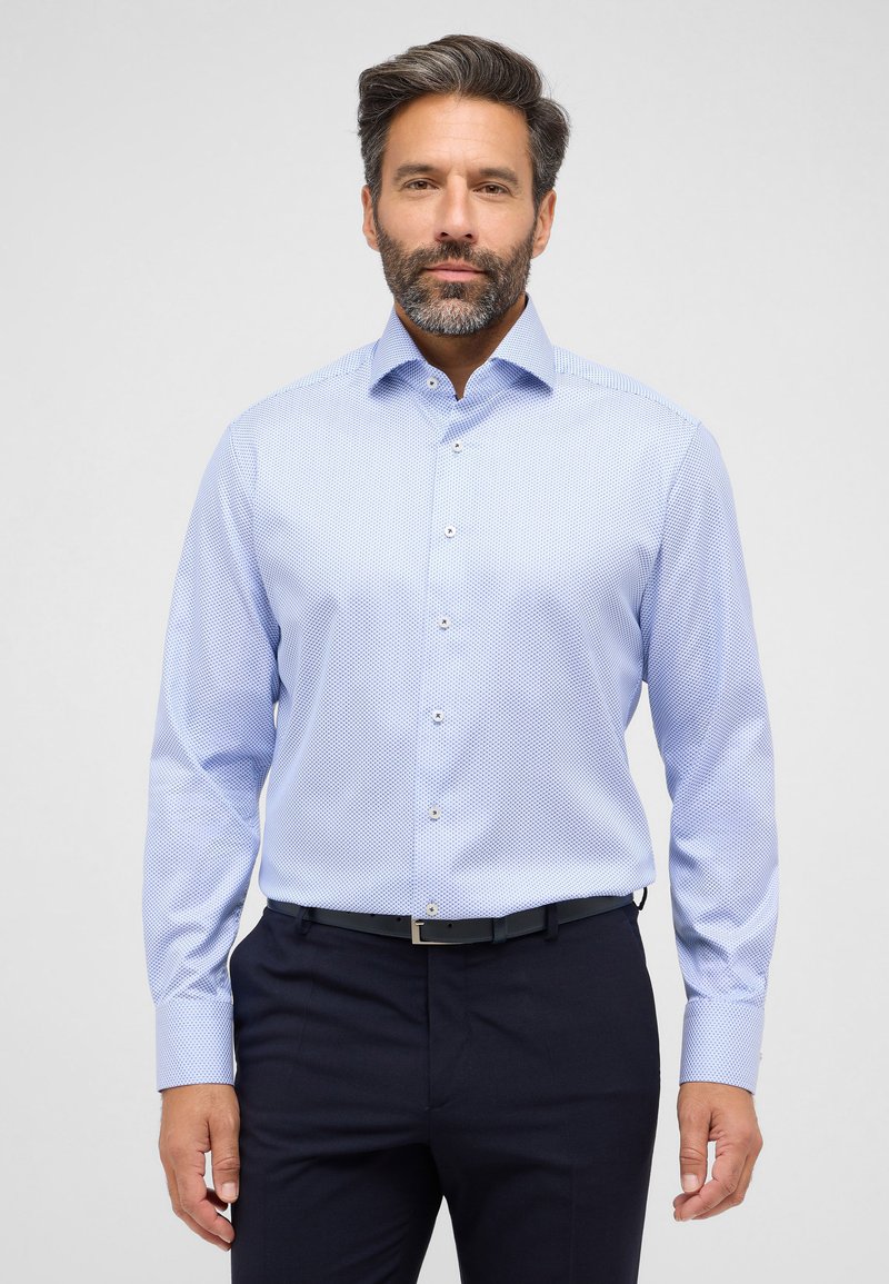 Lichtblauw overhemd met lange mouwen, voorzien van een klein stippenpatroon, puntkraag en knoopsluiting. Draagt met donkere broek, met een strakke riem.