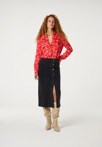 Rode bloemen blouse met knopen, zwarte denimrok met zijsplit en knoopdetail, beige kniehoge haklaarzen.