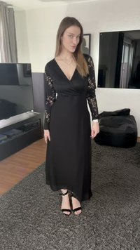 Svart klänning med långa ärmar i spets, V-ringning, flödande form och slät textur. Bärs med svarta remklackar och står på en mörk matta.