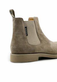 Beige suède enkellaars met elastische zijpanelen, een ronde neus en een gestructureerde rubberen zool met een subtiele hak. Tag zichtbaar aan de zijkant.