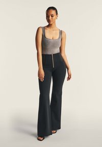 Pantaloni neri a zampa d'elefante con vita alta e dettagli in zip dorato abbinati a un top grigio aderente con scollatura testurizzata.