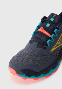 Baskets de sport bleu foncé avec une tige texturée, des accents turquoise, des lacets orange et une semelle multicolore avec un motif de traction rugueux.