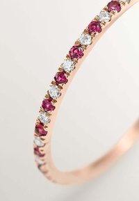Pulsera de oro rosa con una fila de piedras redondas alternas de color púrpura y transparentes, engastadas en un delicado ajuste de garras. Textura suave y forma curva.