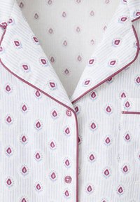 Haut de pyjama blanc avec petit motif floral rouge et bleu, bordure bordeaux, boutons sur le devant et une poche poitrine côté droit.