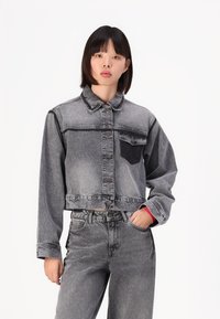 Kuttet denimjakke i grå med en falmet finish, med en mørk brystlomme, knappestolpe og lange ermer. Et par matchende grå jeans.