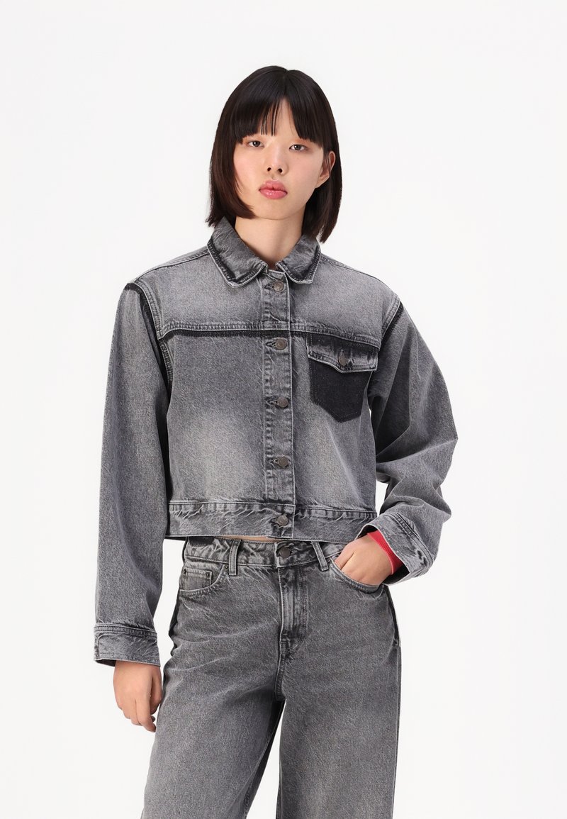Kuttet denimjakke i grå med en falmet finish, med en mørk brystlomme, knappestolpe og lange ermer. Et par matchende grå jeans.