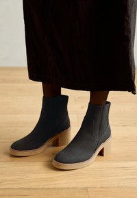 Bottines noires avec une texture en daim lisse, un talon carré et des surpiqûres contrastées. Le design présente des panneaux latéraux élastiques pour un enfilage facile.
