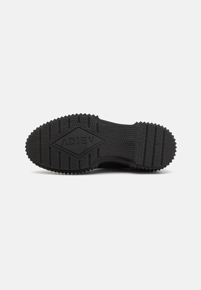 Talpa de sneaker negre cu un model texturat, cu nervuri, logo-ul în relief în centrul său și un material din cauciuc rezistent.