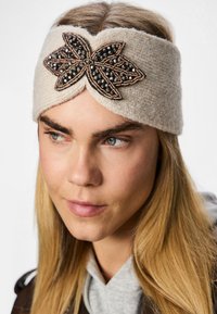 Beežist põimitud peapael, millel on dekoratiivne pruun ja must kaunistatud lillemuster. Sile tekstuur ja mugav istuvus.