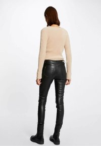 Pull beige en maille duveteuse associé à un pantalon en cuir noir et des bottes noires, présentant une coupe ajustée et des poignets côtelés. Vue arrière montrée.
