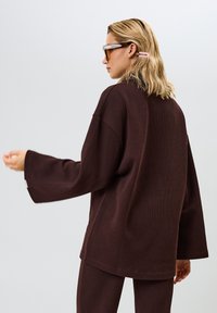 Bruine geribbelde oversized top met lange mouwen, tekstiel met een gestructureerde stof en een losse pasvorm. Accentuated met een klein label voor details, gecombineerd met bijpassende broek.