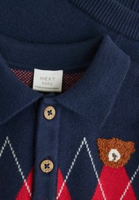 Polo bébé navy avec motif en losanges rouges, featuring des boutons en bois et un ours brodé sur la poitrine. Tissu tricoté doux.