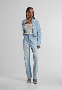 Ljusblå denimjacka med en kortad design, kombinerad med högmidjade ljusblå jeans. Båda har en slät textur och enkel sömnad.