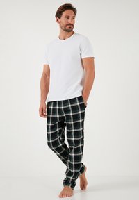 Witte T-shirt met korte mouwen, gecombineerd met donkergroene, zwarte en witte geruite pyjamabroek. De stof lijkt zacht en heeft een relaxte pasvorm.
