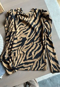Maglia a maniche lunghe in un motivo a strisce tigre marrone e nero, realizzata in tessuto morbido, con scollatura rotonda e spalle leggermente arricciate.