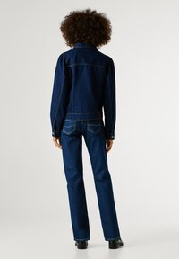 Σκούρα τζιν μπουφάν με φουσκωτά μανίκια, διαθέτει κλασικό γιακά και κουμπιά στους καρπούς, συνδυασμένο με ίσια σκούρα τζιν και μαύρες μπότες.