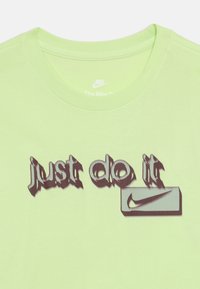 Ανοιχτό πράσινο μπλουζάκι με παραμορφωμένο μαύρο κείμενο "just do it" και το λογότυπο Nike swoosh μέσα σε ένα ορθογώνιο κάτω από το κείμενο.