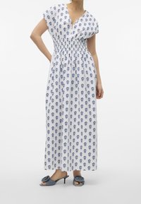 Weißen Midikleid mit Floralprint, kurzen Ärmeln und geraffter Taille. Kombiniert mit blauen High Heels mit floralem Akzent.