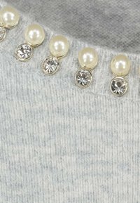 Tessuto grigio lavorato a maglia con elementi decorativi: perle color crema alternate a pietre preziose trasparenti lungo la scollatura, che aggiungono texture e contrasto.