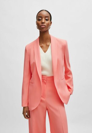 Peach-colored tailored blazer with a shawl collar, paired with matching trousers. Smooth fabric, minimalistic design, featuring side pockets.