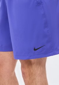 Κοντινό πλάνο στα πόδια ενός ατόμου που φοράει μωβ σορτς Nike με ένα μικρό μαύρο λογότυπο Swoosh κοντά στο τελείωμα στη δεξιά πλευρά.