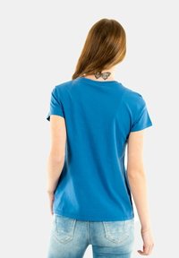 Camiseta de algodón azul con un escote redondeado y mangas cortas, con una textura suave. La vista trasera muestra un tatuaje de mariposa.