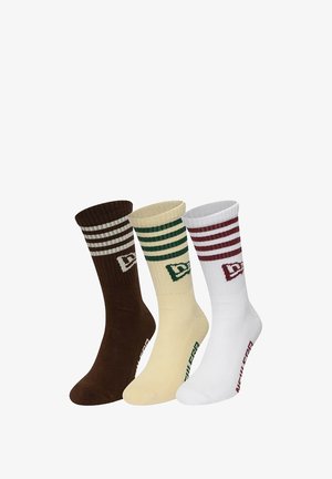 Set aus drei Crew-Socken in Braun, Gelb und Weiß. Jede Socke hat einen gerippten Bund, kontrastierende Streifen und ein Logo-Detail nahe dem Knöchel.