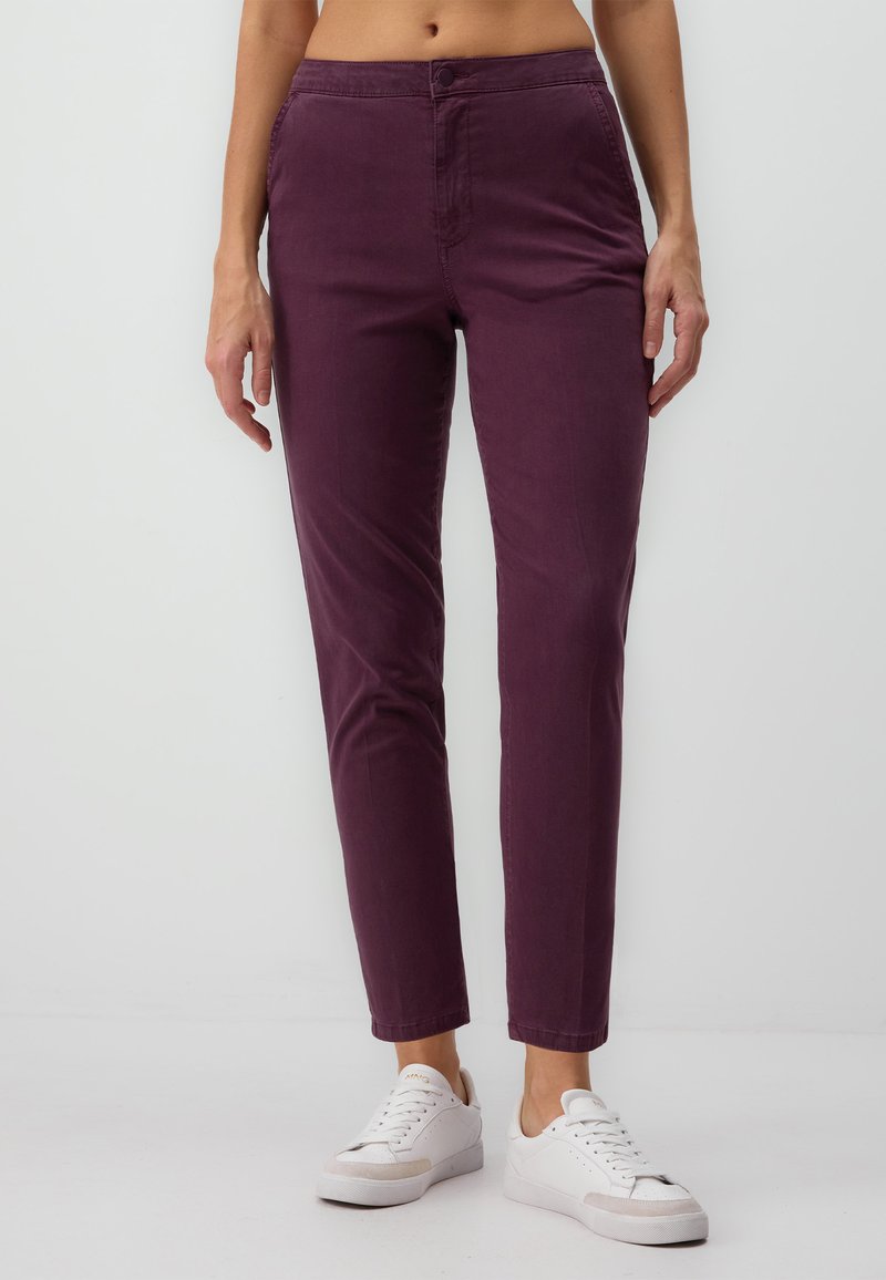 Pantalons ajustés bordeaux en coton, avec fermeture à bouton, poches avant et longueur courte, associés à des baskets blanches.