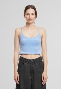 Top corto de color azul claro con tirantes finos, hecho de un tejido suave. Combinado con pantalones de pierna ancha negros de talle alto que cuentan con bolsillos.