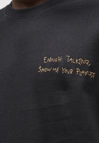 Μαύρο φούτερ με στρογγυλή λαιμόκοψη, διακοσμημένο με κεντημένο χρυσό κείμενο: «Φτάνει η ομιλία, Δείξε μου τη λίστα αναπαραγωγής σου.» Απαλή υφή υφάσματος.