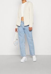 Blazer court crème avec un seul bouton, jean taille haute bleu clair, baskets blanches à plateforme, et petit sac à bandoulière à motif.