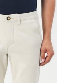 Beige katoenen blend chinos met een voorzak, knoopsluiting en slim fit. Geverfde stof met een gladde afwerking.