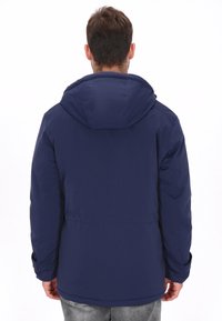 Chaqueta con capucha azul marino de textura suave, puños elásticos y ajuste relajado. Presenta una cintura entallada y un diseño minimalista.