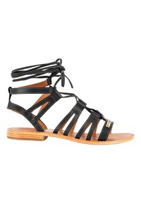 Zwarte leren sandalen met uitsnijdingen en enkellussen. Platte houten zool met minimale hak. Contrasterende stiksels en gouden accentdetails.