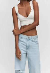 Top corto de punto blanco con escote en V profundo y bordes festoneados, combinado con jeans de tiro alto de pierna ancha en un tono azul claro y desgastados.
