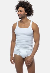 Top in cotone bianco senza maniche con scollatura quadrata e spalline larghe, abbinato a mutandine in cotone bianco, che mostrano una texture liscia e un design aderente.