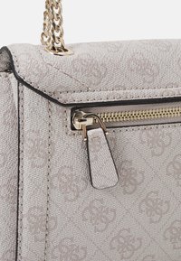 Beige textured handbag with embossed pattern, gold hardware, chain strap, and zippered compartment. Compact rectangular shape.