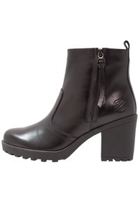 Bottes chevilles en cuir noir à finition lisse, fermeture éclair latérale, talon épais et semelle en caoutchouc texturée. Détail du logo embossé sur le côté.
