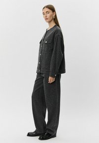 Črna denim jakna z leopardjim vzorcem, ki ima gumbe in dva žepka na prsih, v kombinaciji z usklajenimi širokimi hlačami in poliranimi čevlji.