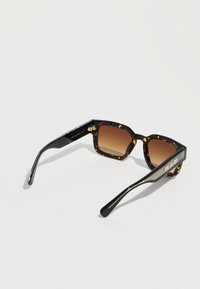 Pravokotna sončna očala s tortoiseshell okvirjem, z rjavimi lečami z gradacijo in črnimi kraki z zlatimi poudarki na svetlem ozadju.