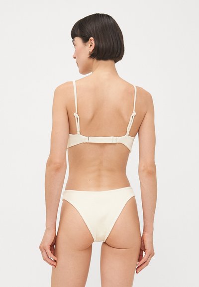 Krēma krāsas ribota bikini komplekts ar plānām regulējamām siksniņām un āķa aizdari aizmugurē. Augsta jostasvietas apakšdaļa ar minimālu segumu.