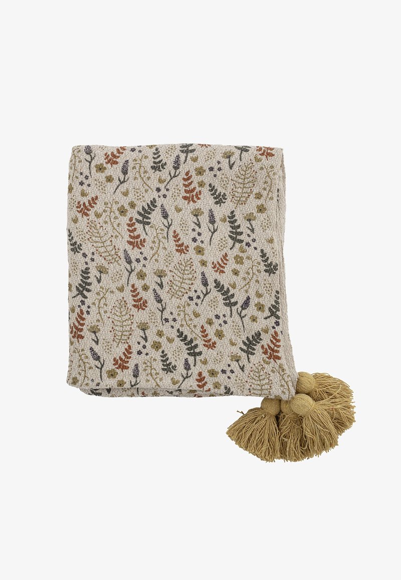 Tissu beige plié avec des motifs floraux et feuillus multicolores et quatre grands pompons couleur sable dans un coin.