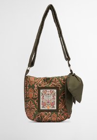 Zielona torba na ramię z tkaniny charakteryzuje się skomplikowanym wzorem w koralowy, prostokątną łatką z logo i przewiązaną ozdobą. Wykonana z pikowanej materiału.