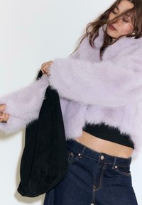 Lavendel faux fur cropped jakke med brede ærmer, parret med en sort suedetaske og mørke denimjeans med kobberdetaljer.