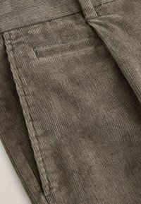 Samthose in Olivgrün mit gerippter Textur, Seitentasche und gestickten Details entlang der Nähte.