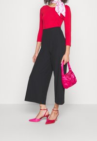 Červený top s dlouhým rukávem, černé široké kalhoty, růžová saténová kabelka a růžové vysoké podpatky s otevřenou patou a tenkými pásky.