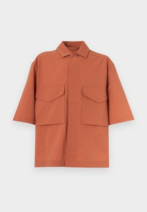 Chemise à manches courtes de couleur rouille avec de grandes poches à rabat des deux côtés, un col pointu et une patte de boutonnage cachée à l'avant.