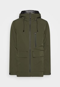 Giacca impermeabile verde oliva con cappuccio foderato in nero, zip frontale, due ampie tasche e regolazioni con cordino. Presenta cuciture geometriche.