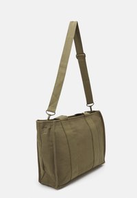 Prostokątna torba płócienna w oliwkowym kolorze z dwiema pionowymi rączkami i regulowanym paskiem na ramię, pokazana na białym tle.